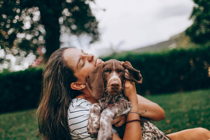 Mulher a abraçar um cachorro sentada num jardim
